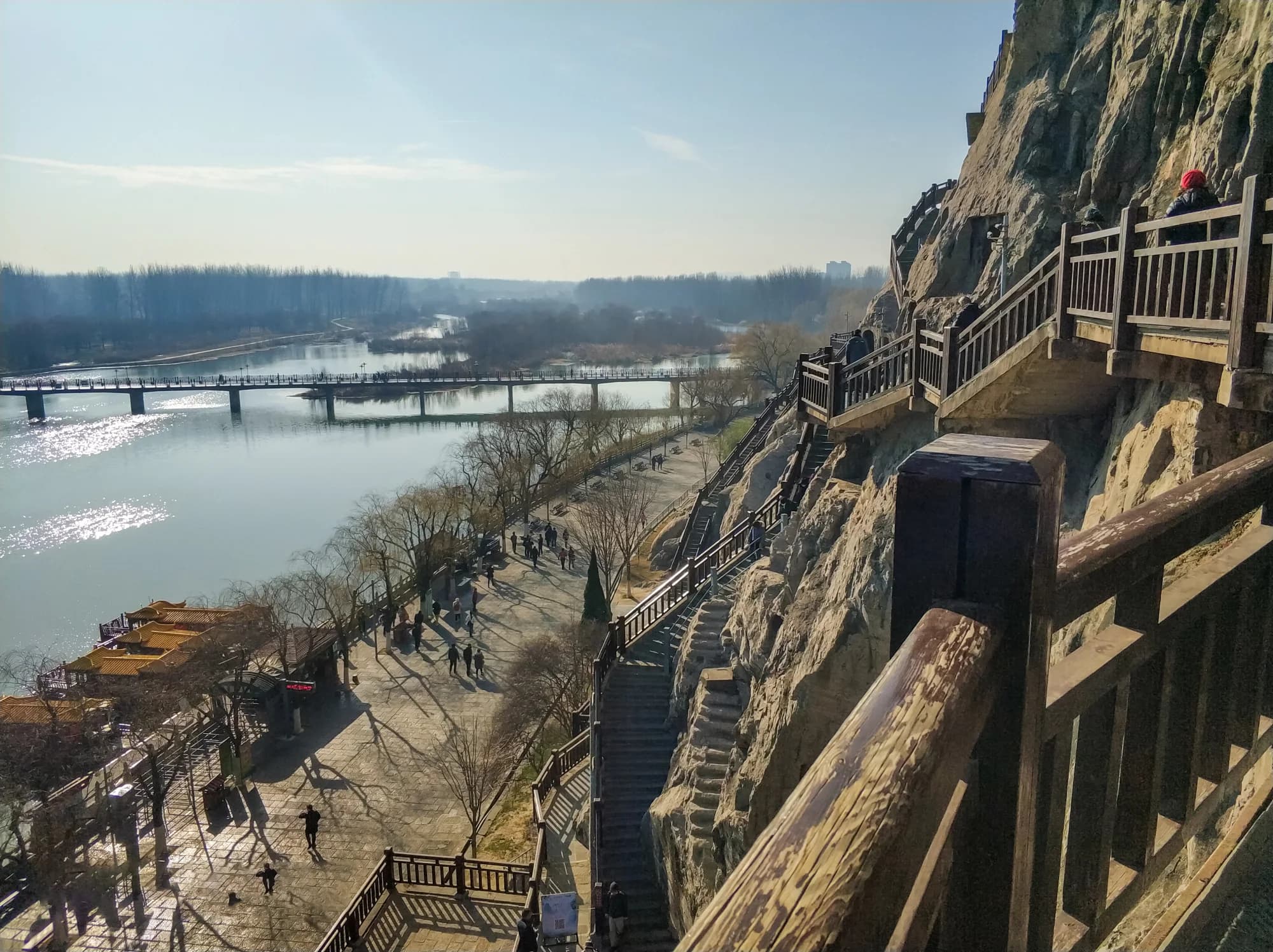 Longmen Grottoes cliff, riverside walkway and Yi River under a clear sky in Luoyang