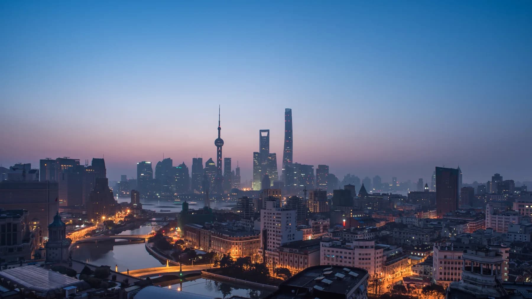 Shanghai at dusk with the historic Bund, Huangpu River and Pudong skyline visible in one urban panorama