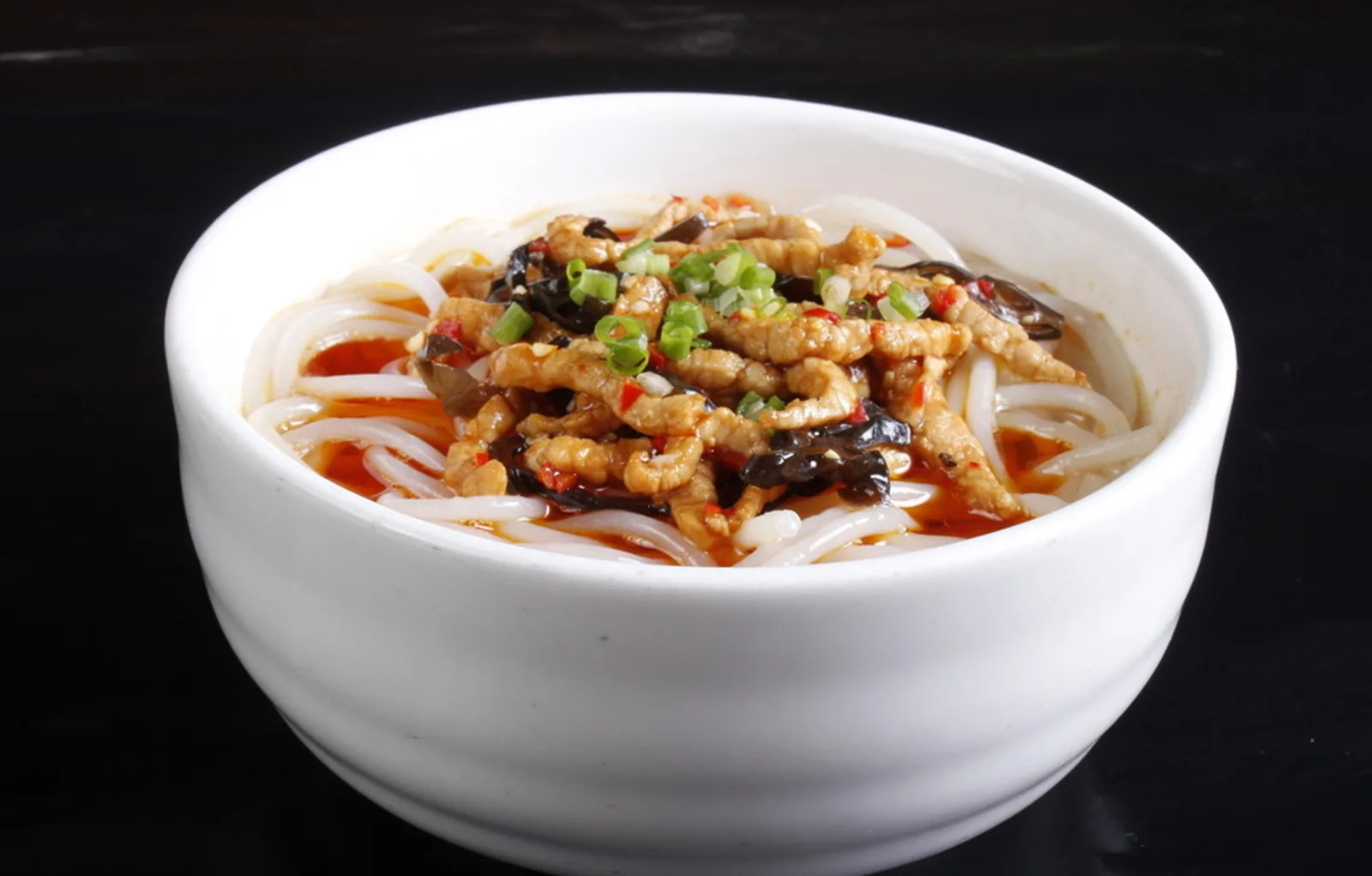 A bowl of Hunan rice noodles topped with pork, wood ear, scallions and red chili