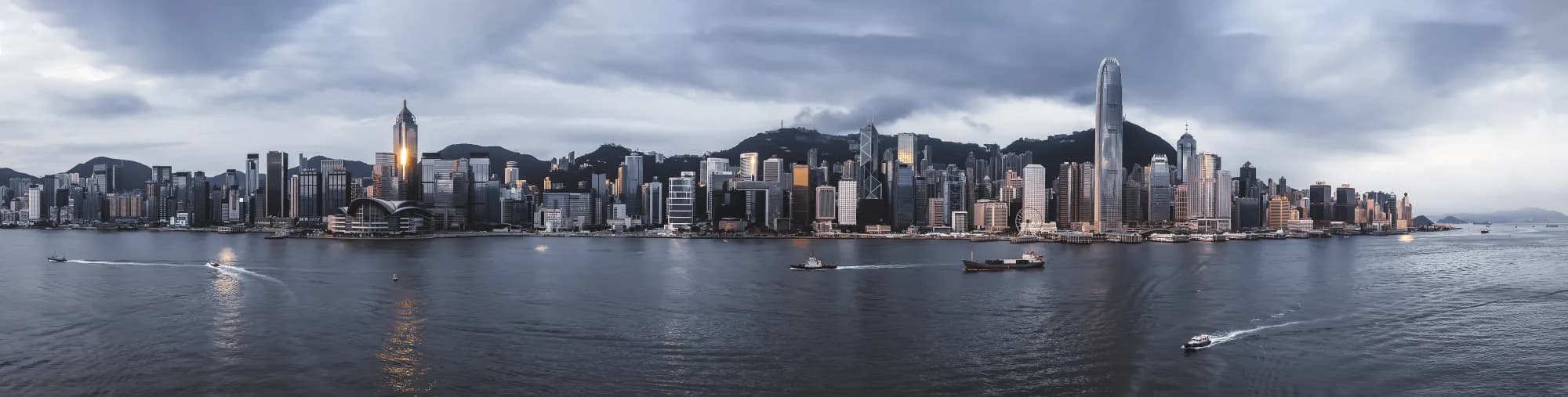 Wide sunrise panorama of Victoria Harbour with Hong Kong Island's skyline, green hills and working boats