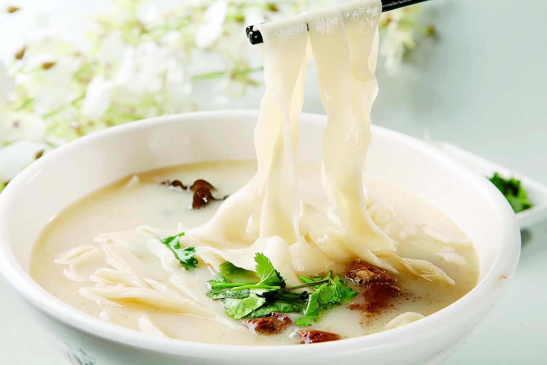 A bowl of Henan huimian with broad hand-stretched noodles, broth, mushrooms and greens