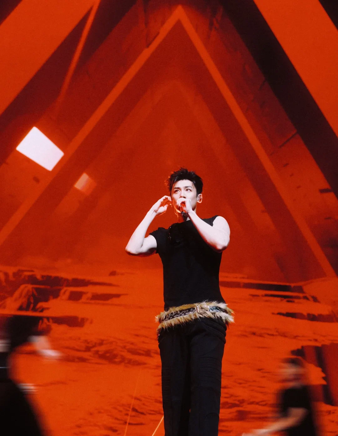 Bai Jingting holding a microphone on a red-lit stage in a July 2026 official studio photograph