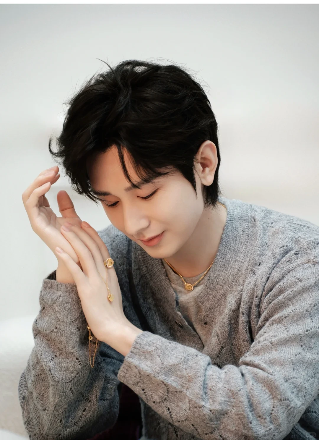 Cheng Yi in a contemporary CMOStudio portrait wearing a grey knit top and looking down with his hands raised near his face