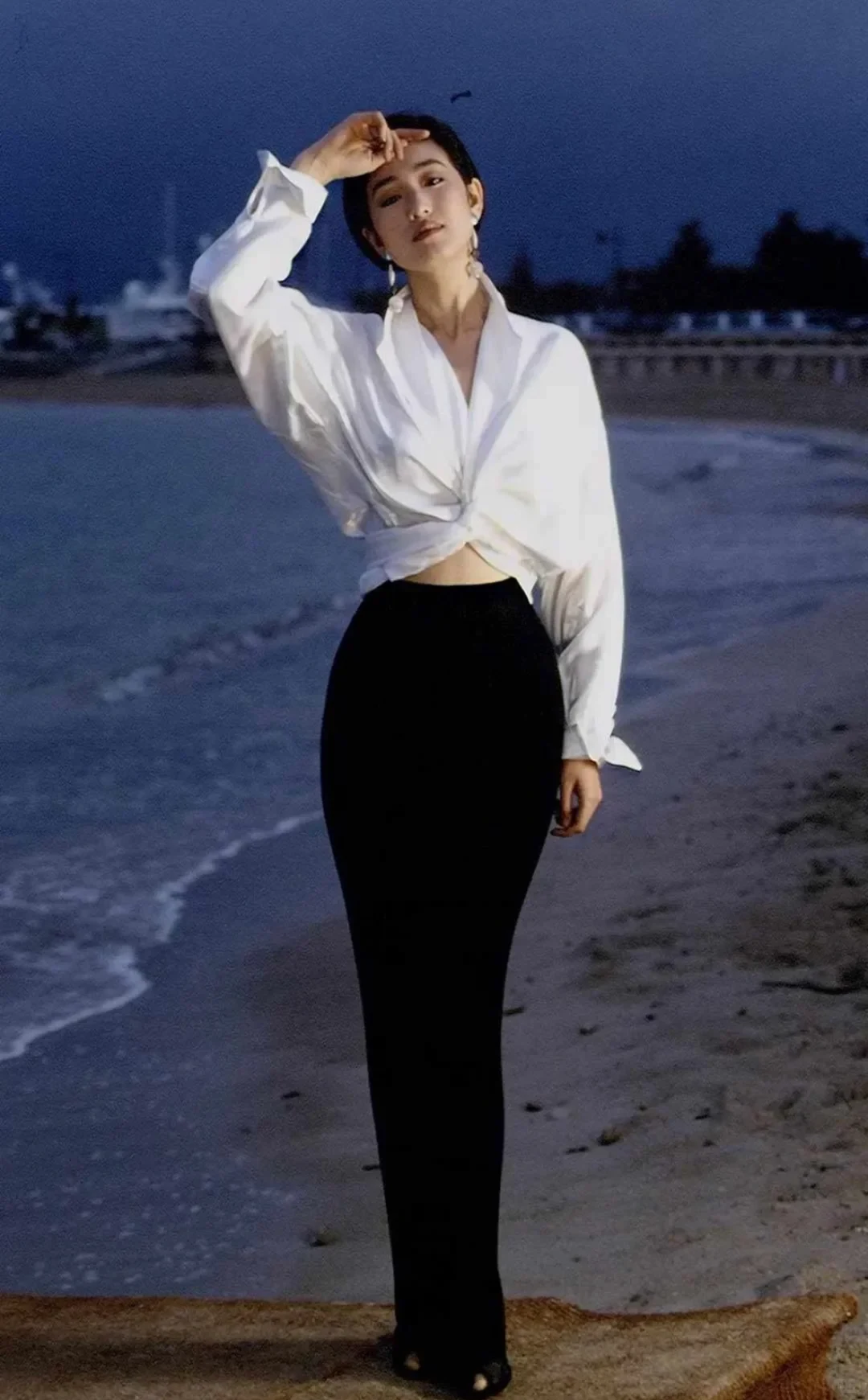 Gong Li in a white shirt and black trousers during the 1993 Cannes period, standing beside the sea