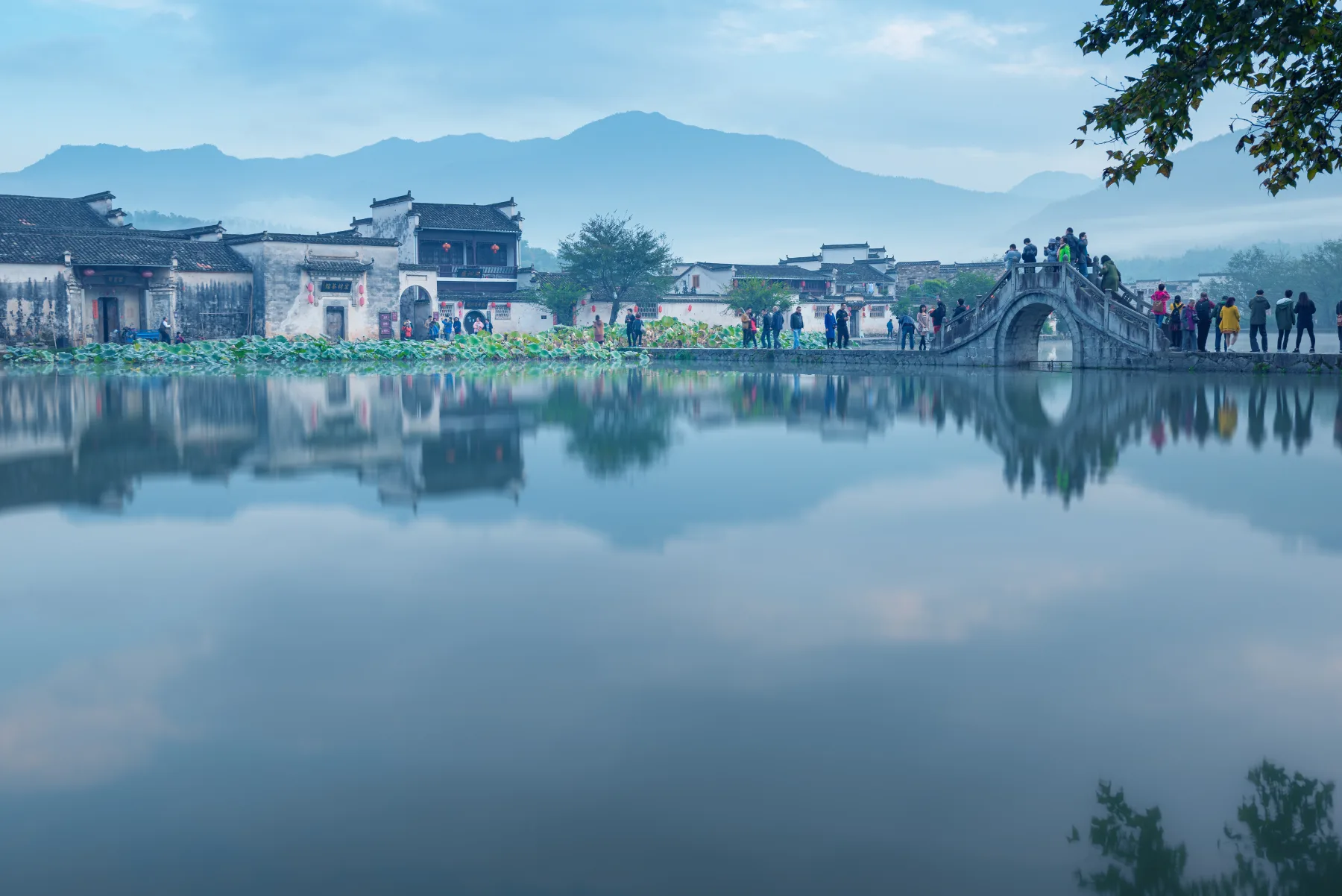 Traditional Chinese architecture in Hongcun with white-walled houses, dark tiled roofs, a stone bridge and water reflecting the village