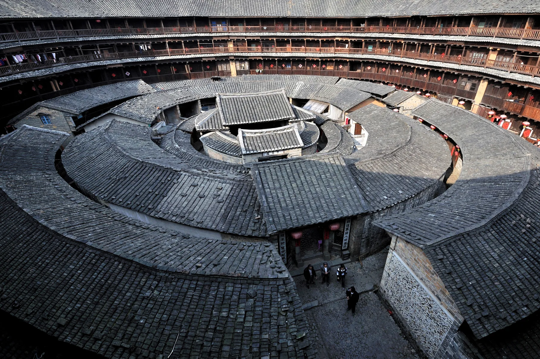 Traditional Chinese architecture inside a circular Fujian tulou with concentric tiled roofs surrounding a shared courtyard