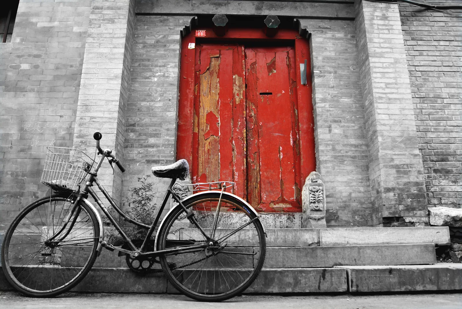 A bicycle beside a gray-brick hutong wall and red courtyard door in Beijing