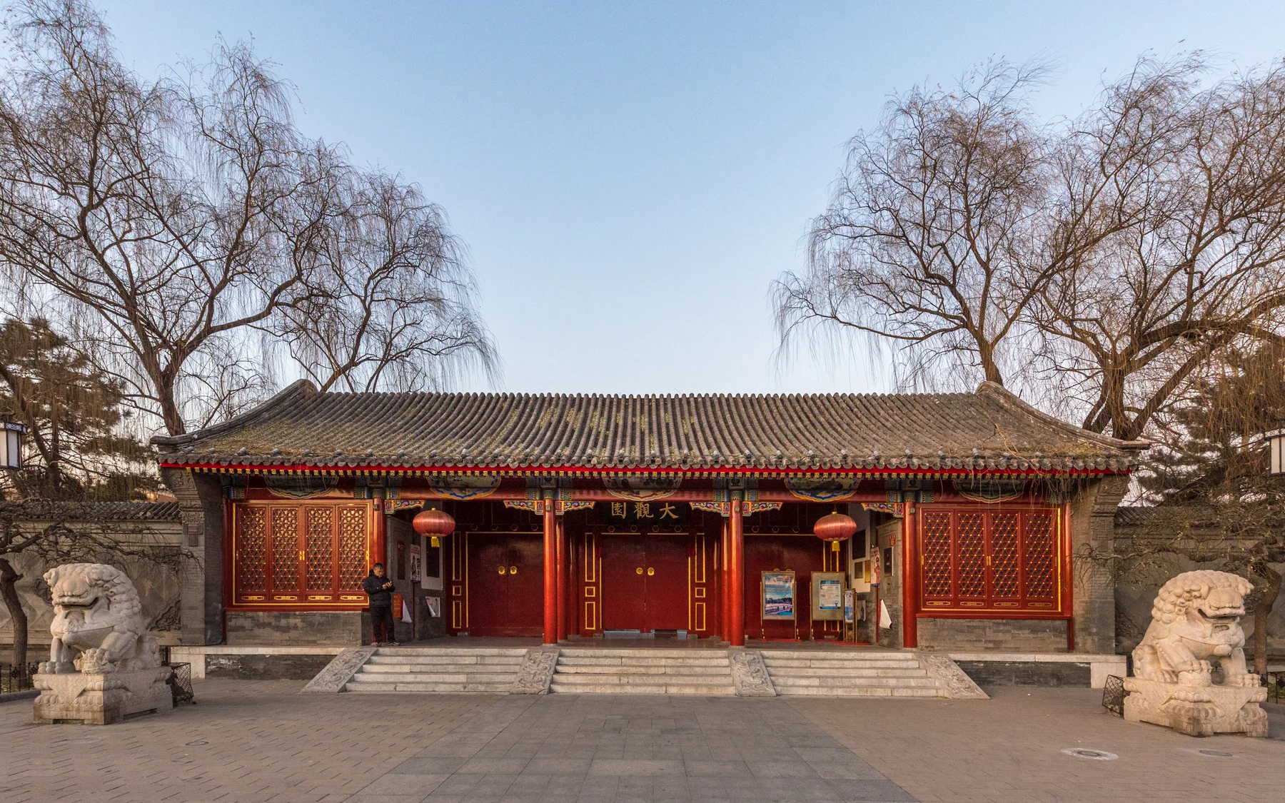 A Beijing courtyard threshold with a red timber gate, gray brick walls and stone guardian lions