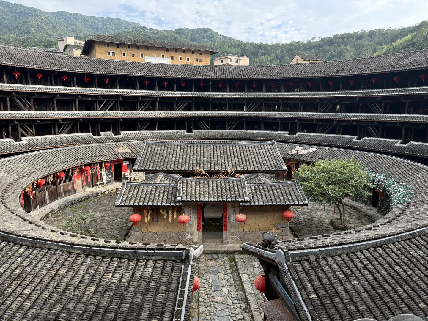 A lived Fujian tulou courtyard with stacked timber galleries, tiled roofs, lanterns and working ground-floor rooms