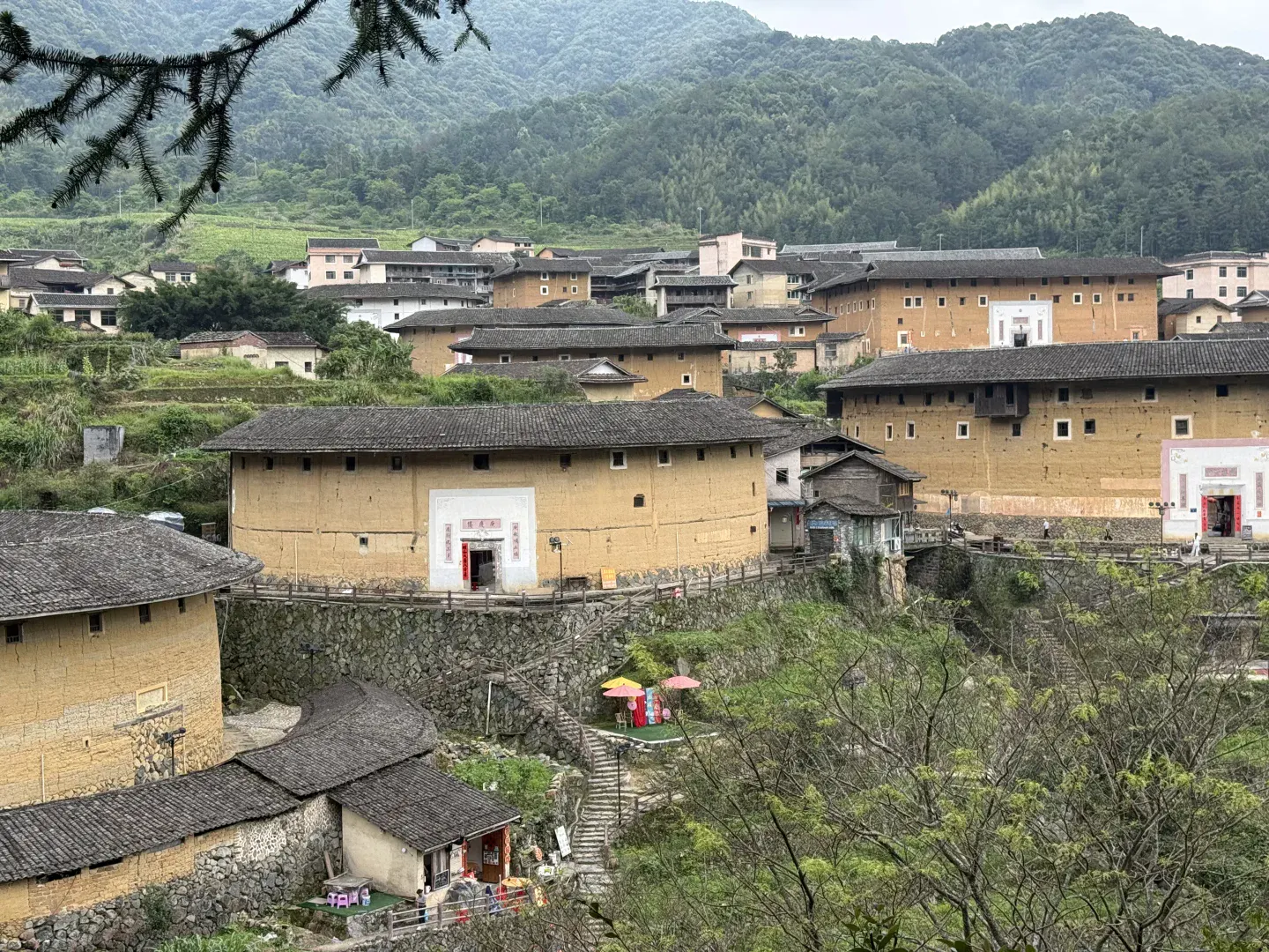 Multiple Fujian tulou and neighboring houses arranged across a green mountain settlement rather than standing as an isolated monument