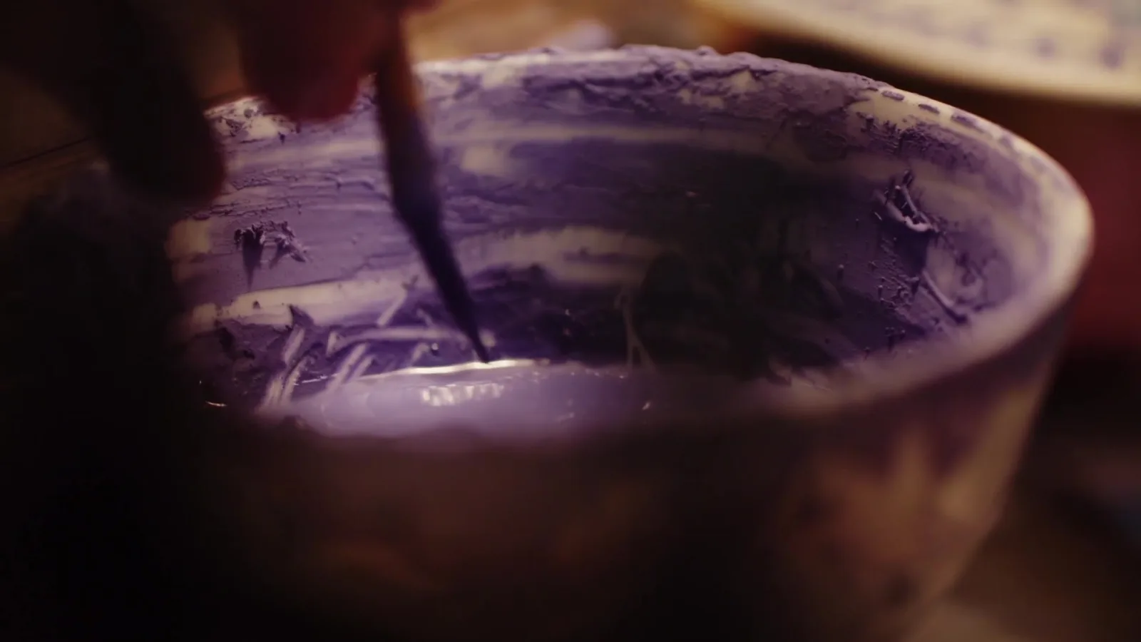 A brush moving through dark cobalt-bearing ceramic pigment before blue-and-white porcelain firing