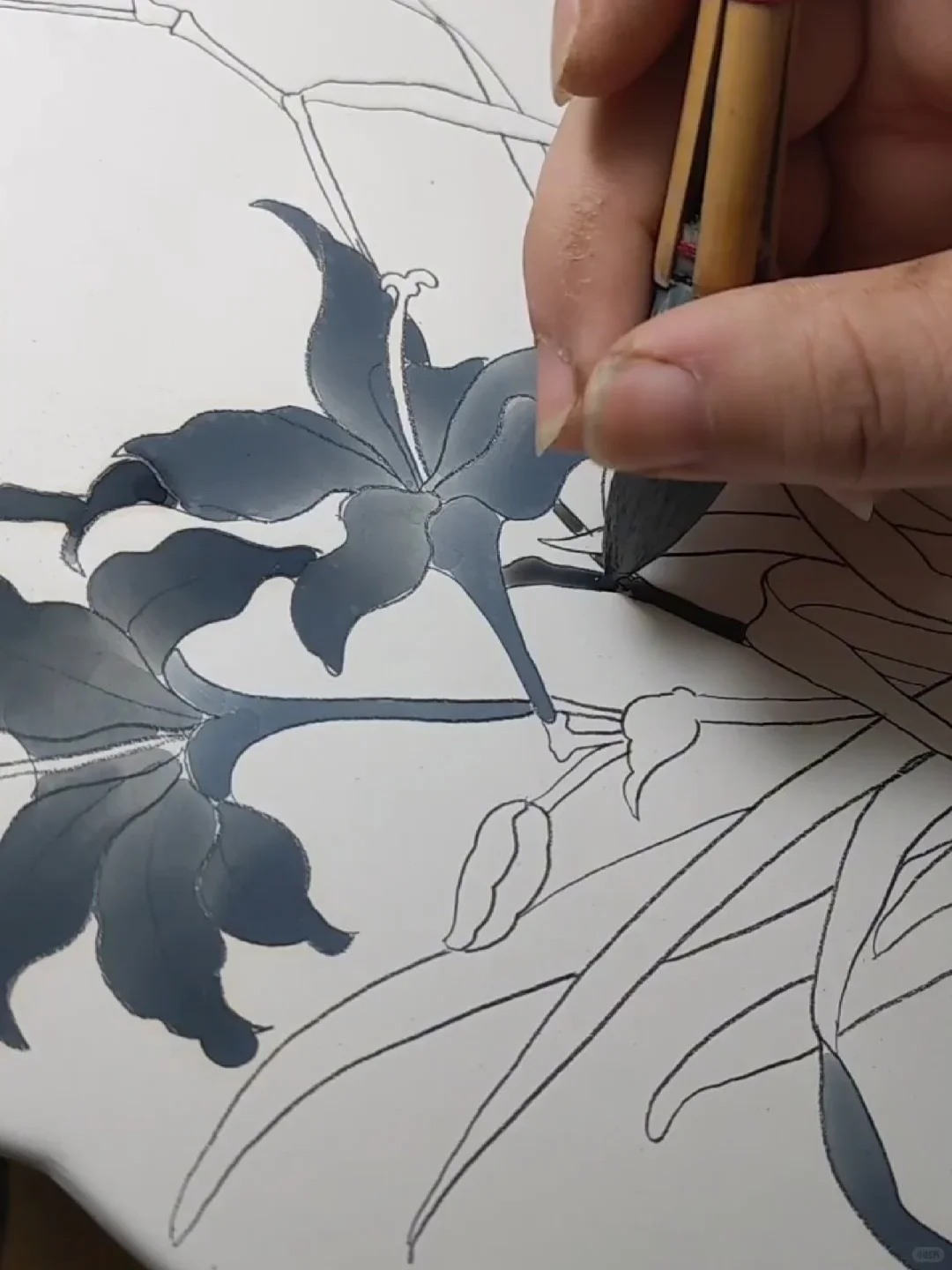 A porcelain painter using a broad brush to fill outlined leaves with graded gray-blue washes before firing