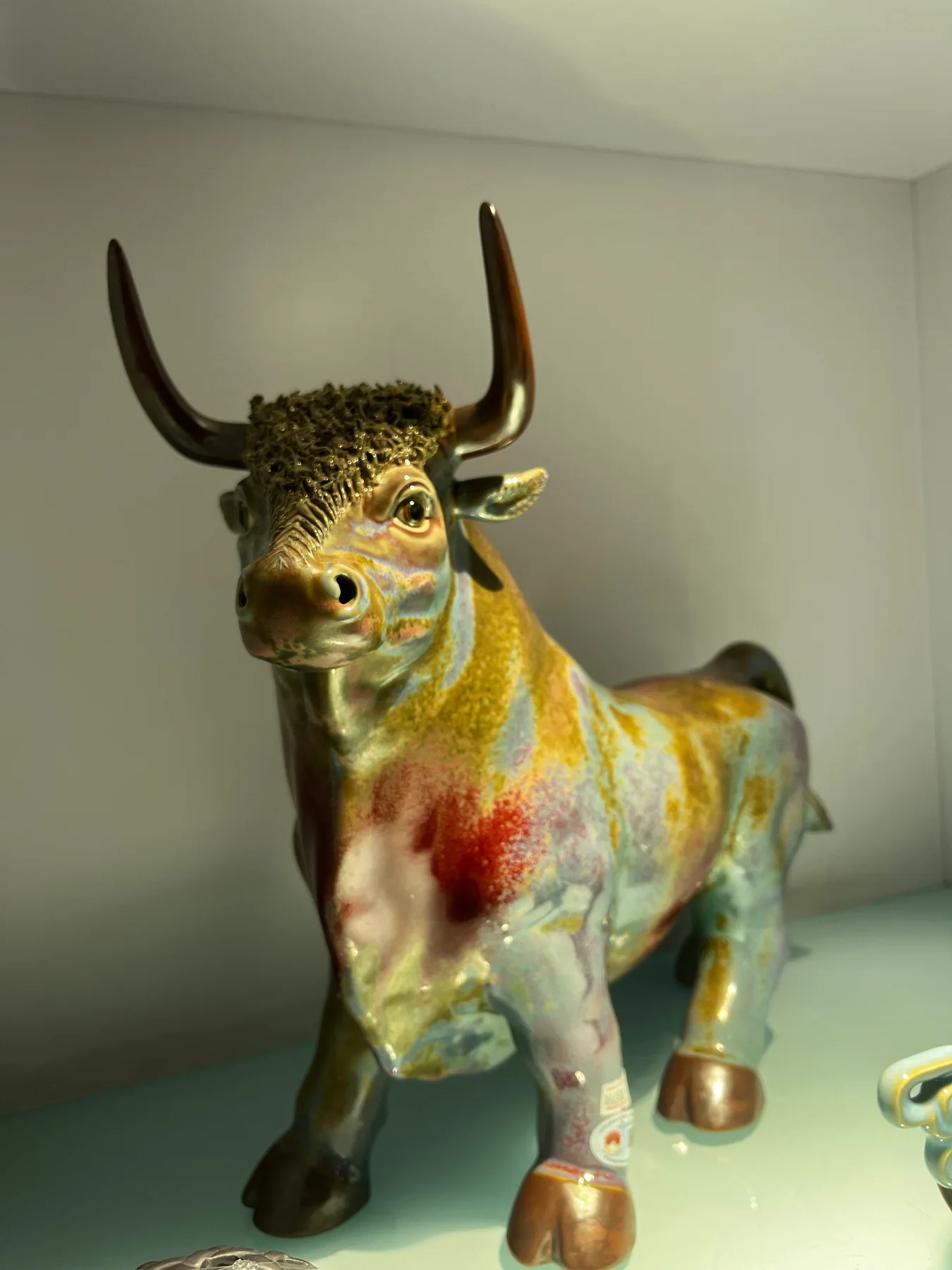 Glazed ceramic bull sculpture with pointed horns and contrasting warm and cool areas across its body