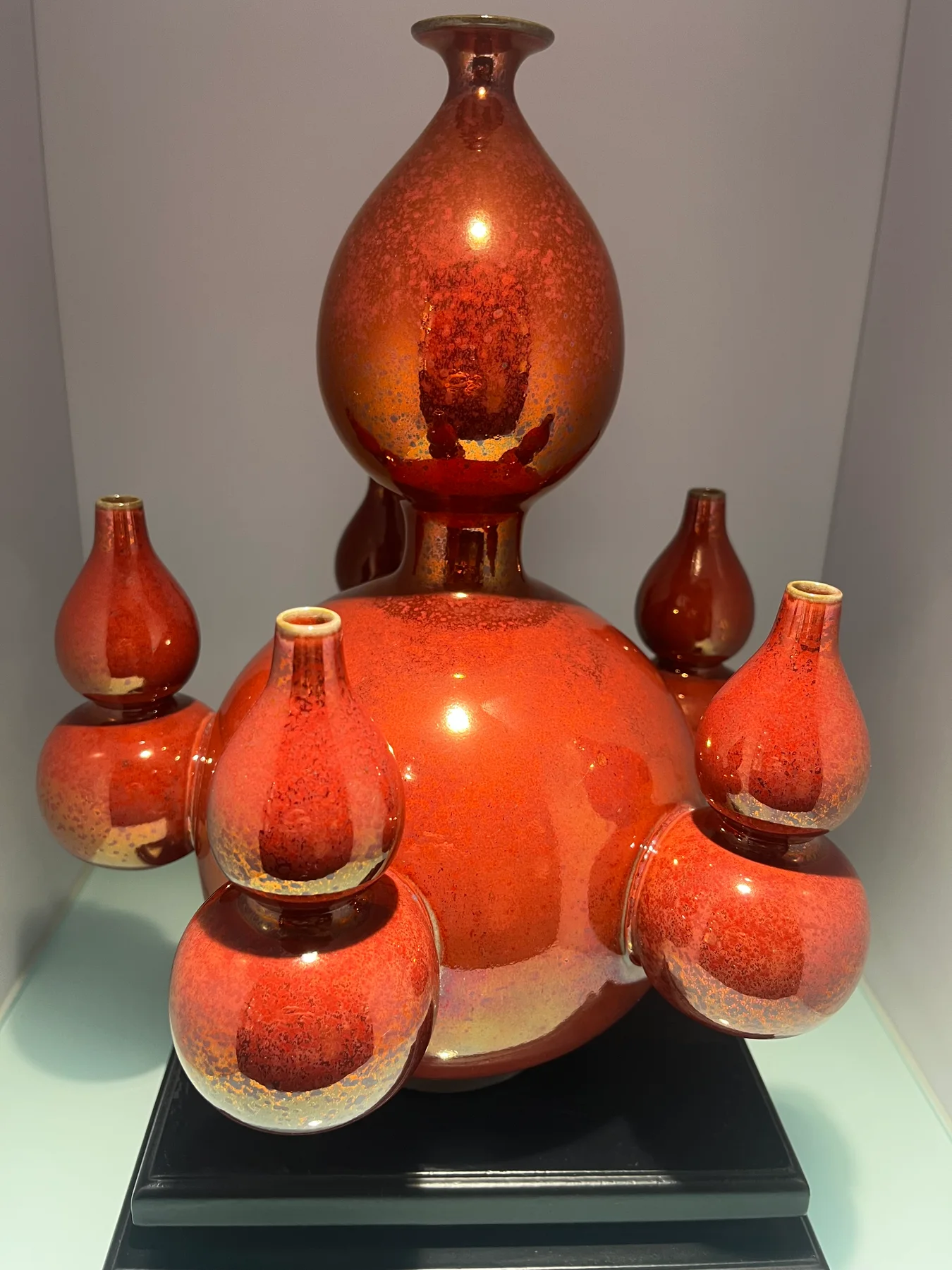 Group of red-glazed ceramic vessels arranged at different heights around a tall narrow-necked form