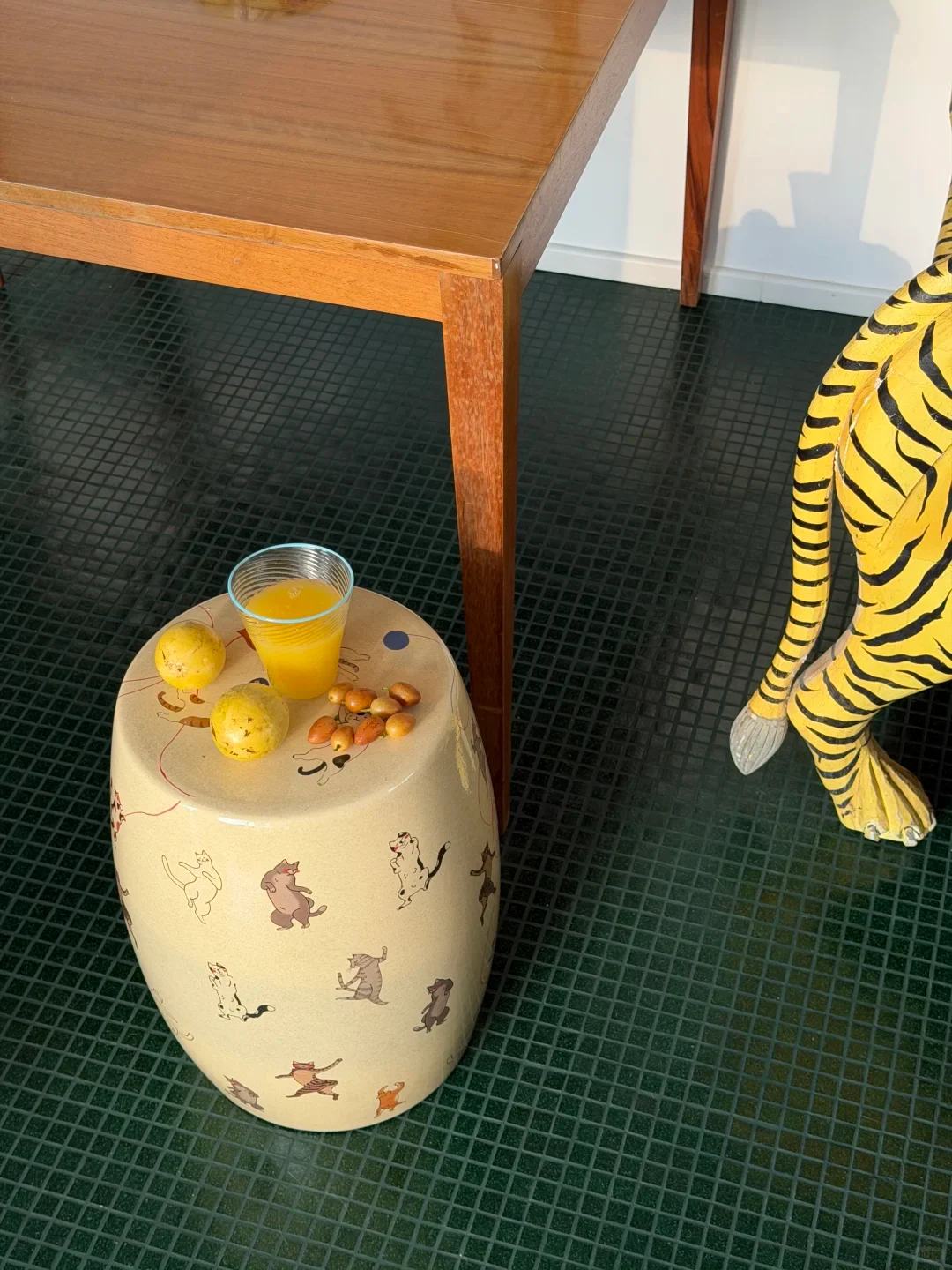 A glass of tea and small items occupy the round top of a cat-painted ceramic stool
