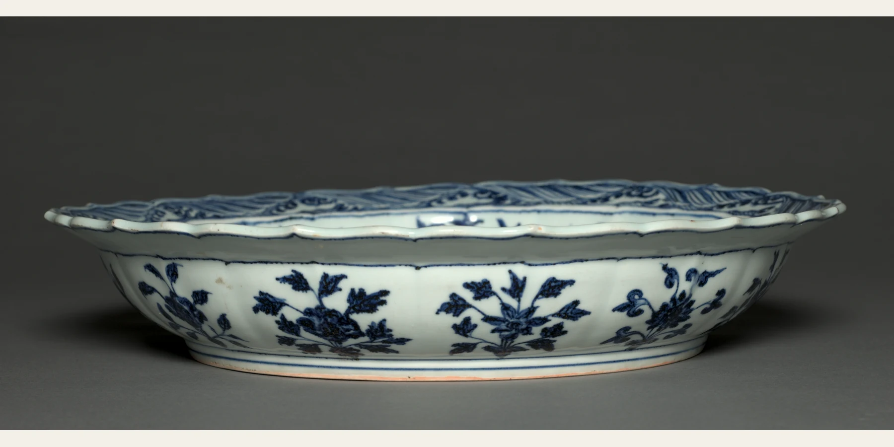 A large Yongle-period Jingdezhen porcelain plate seen from a low angle, revealing its rim, sloping interior, well and raised foot