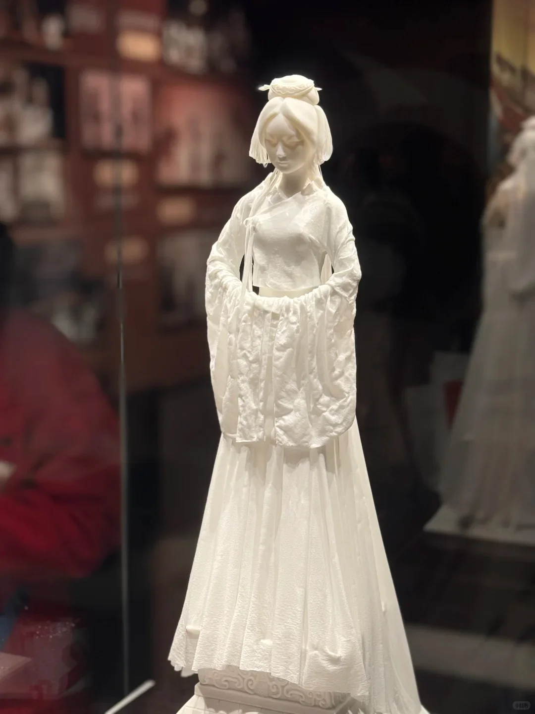 Contemporary white porcelain female figure with long finely modeled sleeves and a pleated dress in a museum display