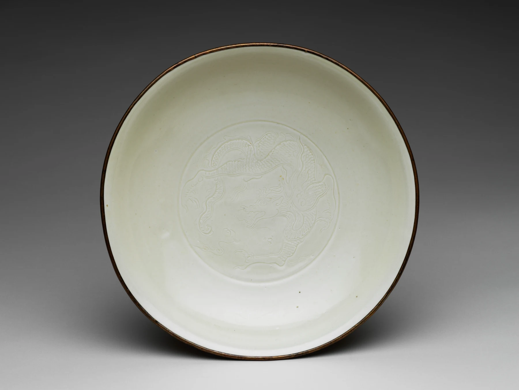 Ding ware dish with an incised dragon beneath ivory glaze and a dark metal-bound rim