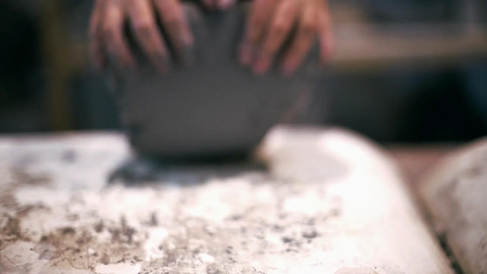 A ceramic worker wedging pale clay on a workshop table before porcelain forming begins