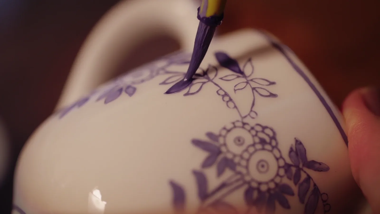 A painter guiding a fine blue line across the curved white surface of a Chinese porcelain vessel