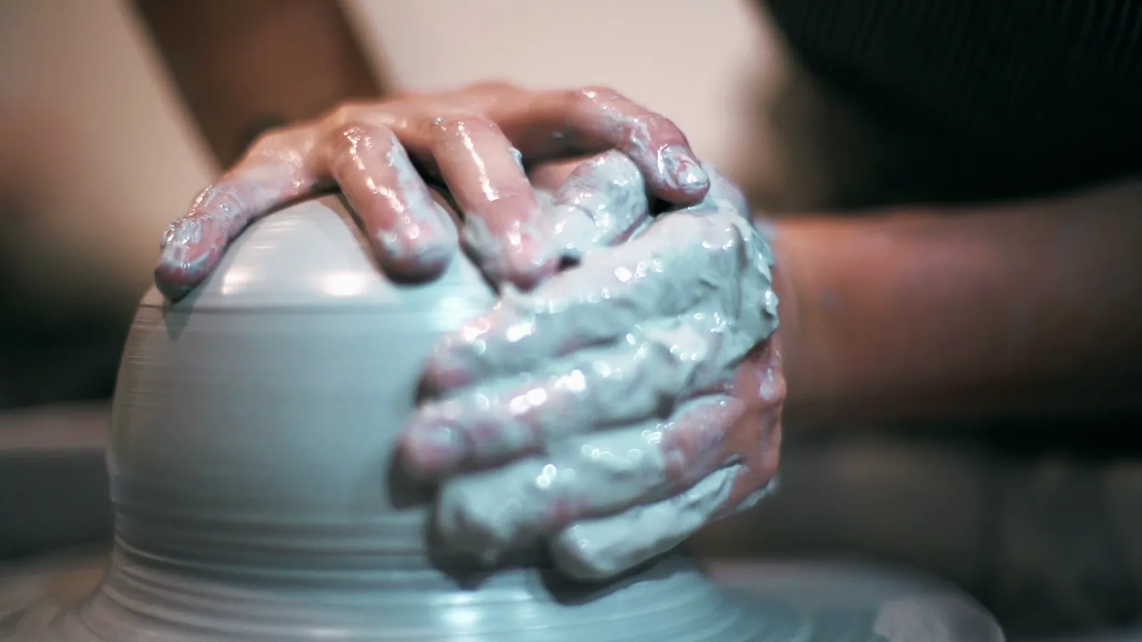 Wet porcelain clay rising between a potter's hands as the wheel establishes a symmetrical form