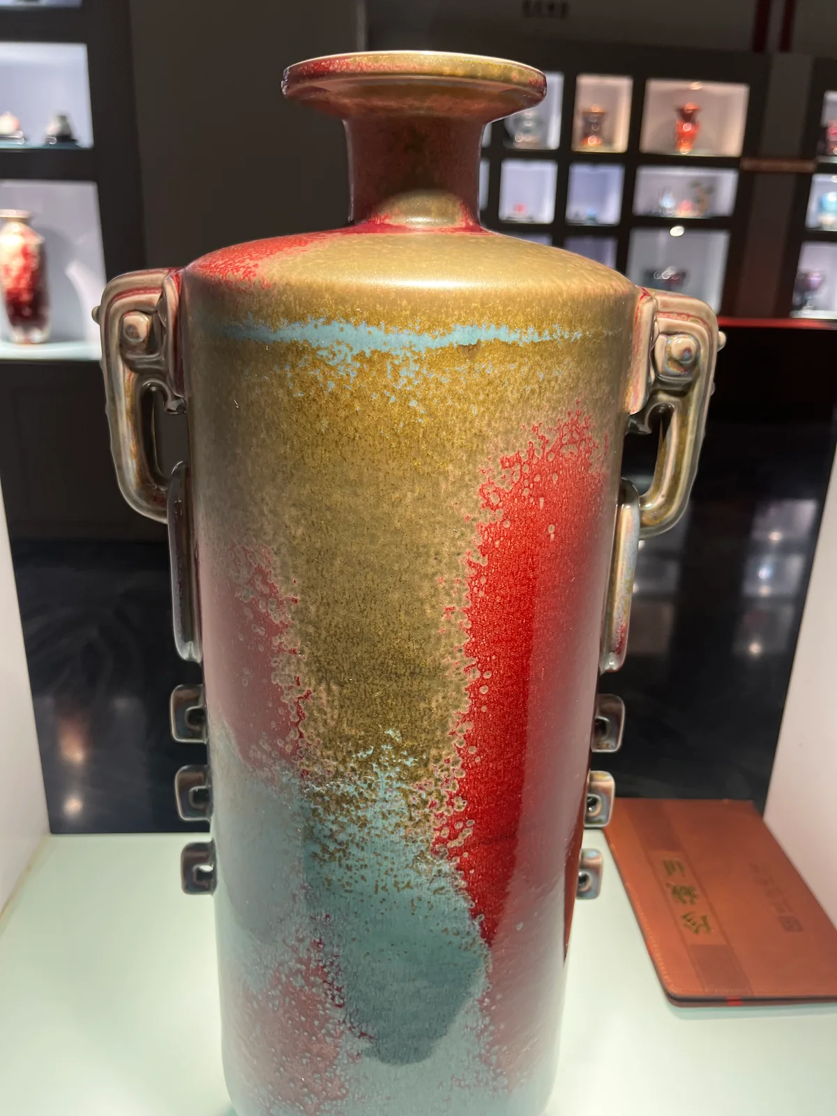 A contemporary Jun-style cylindrical vessel with red, ochre and blue-green glaze fields