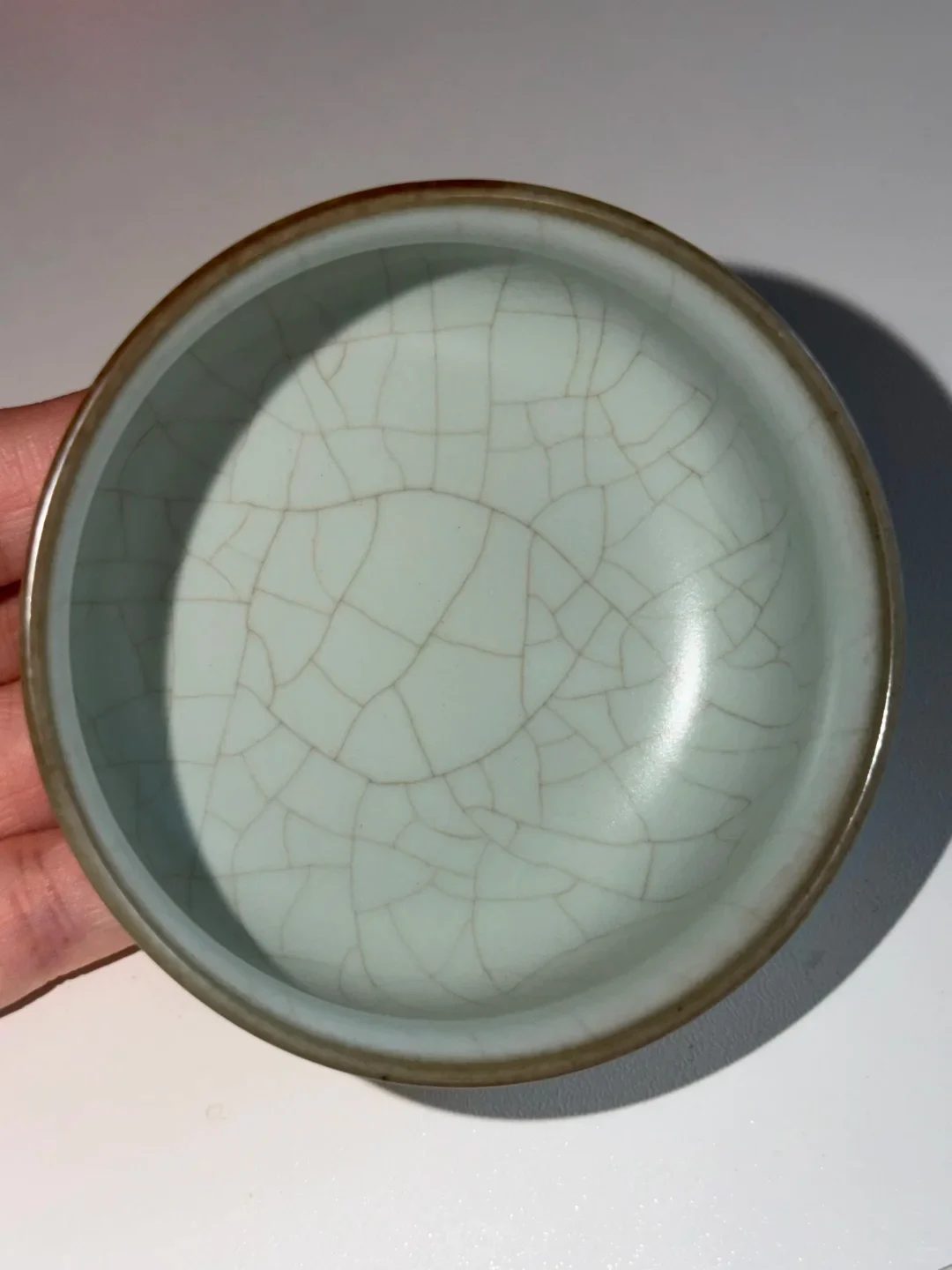 Modern Ru-style cup held in a hand, with fine dark lines visible across its pale green interior