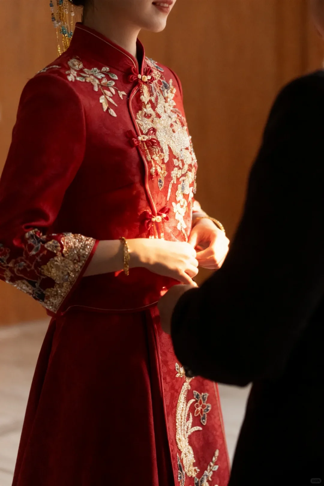 Close view of a contemporary red Chinese wedding jacket showing collar piping, knotted fastenings and dense metallic embroidery