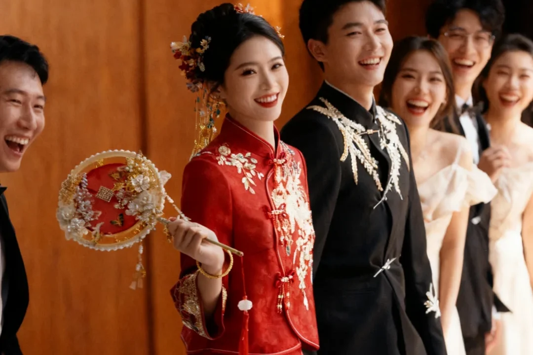 A bride in a red embroidered Chinese wedding dress laughing with the groom and friends