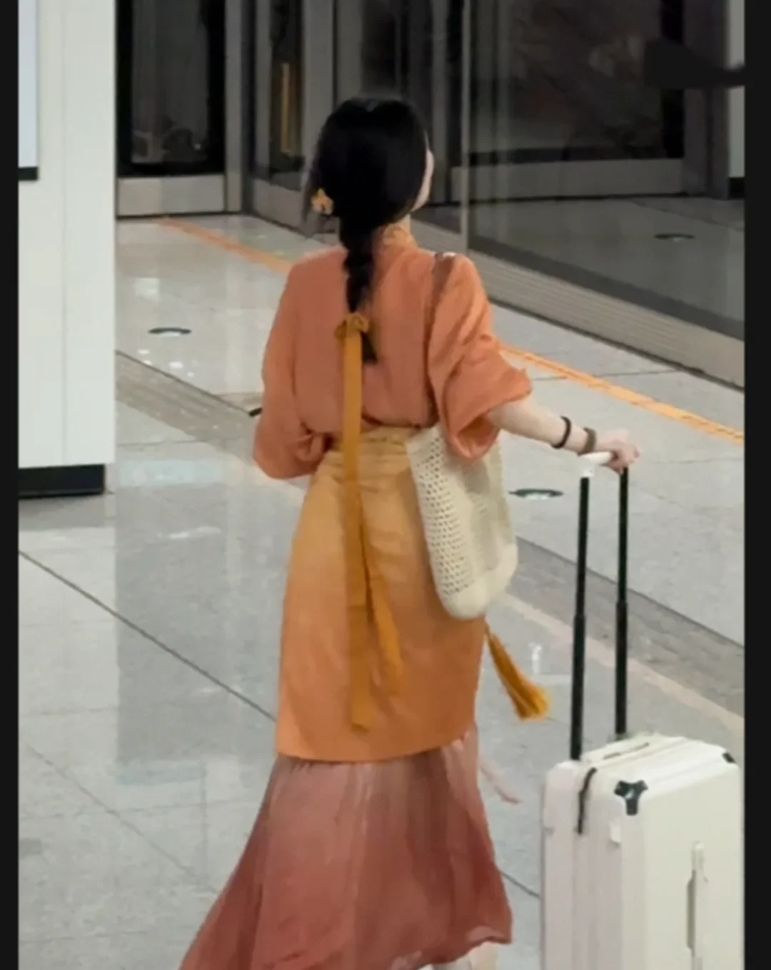 A Hanfu wearer pulling a suitcase through a modern metro station