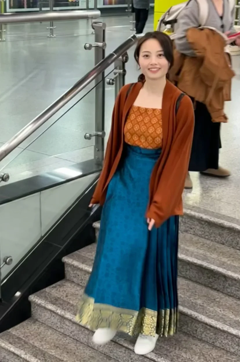 A woman in a rust knit Song-inspired top, blue mamian skirt and white sneakers walking through a modern metro station