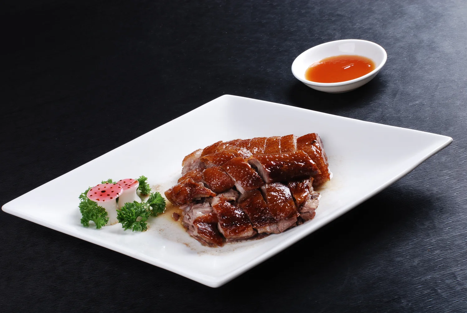 Chopped Cantonese roast goose served beside its dipping sauce, with lacquered skin and the cut meat visible together