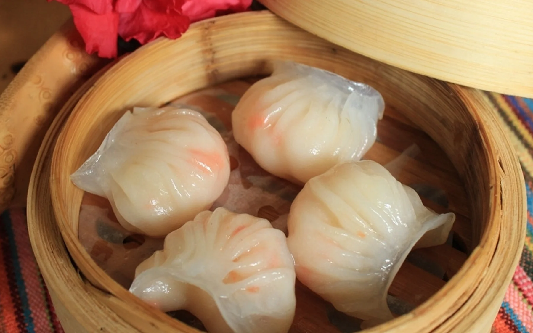 Four har gow in a bamboo steamer, making wrapper translucency and repeated pleating easy to compare at the table