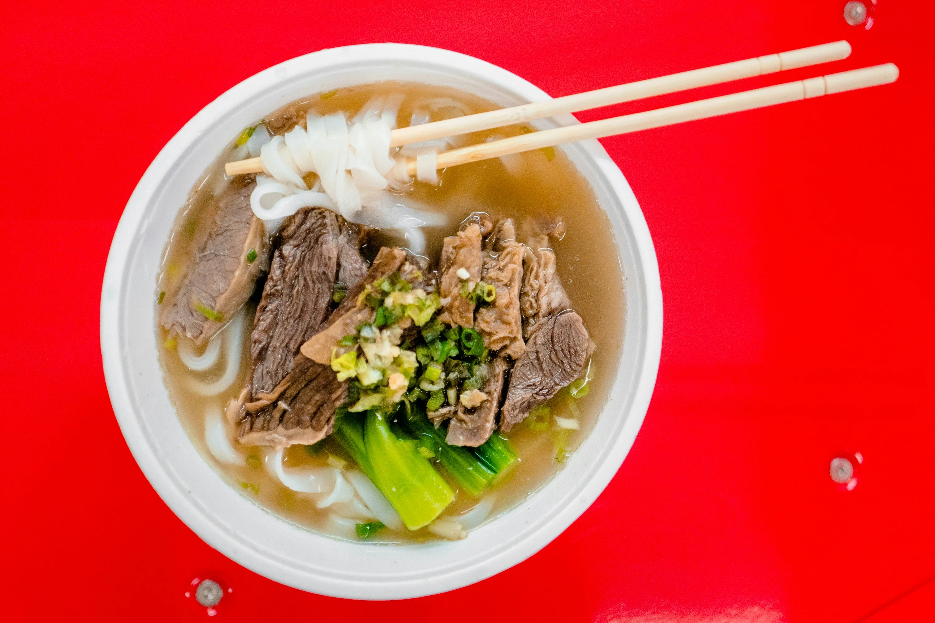 A bowl of wheat noodles with sliced meat and greens representing the everyday reach of popular Chinese food