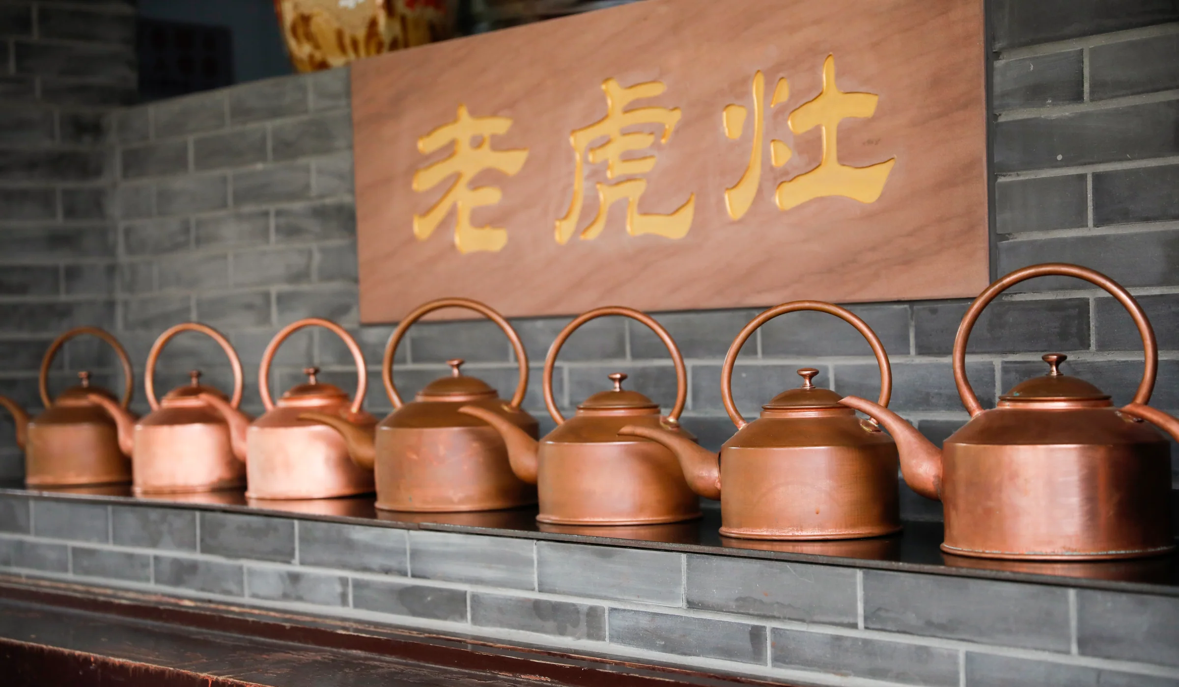A row of copper kettles at a working Chengdu teahouse beneath the Chinese words for tiger stove
