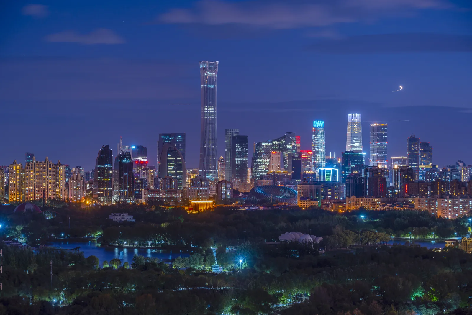 The contemporary Beijing skyline illuminated at night beyond a dark urban park