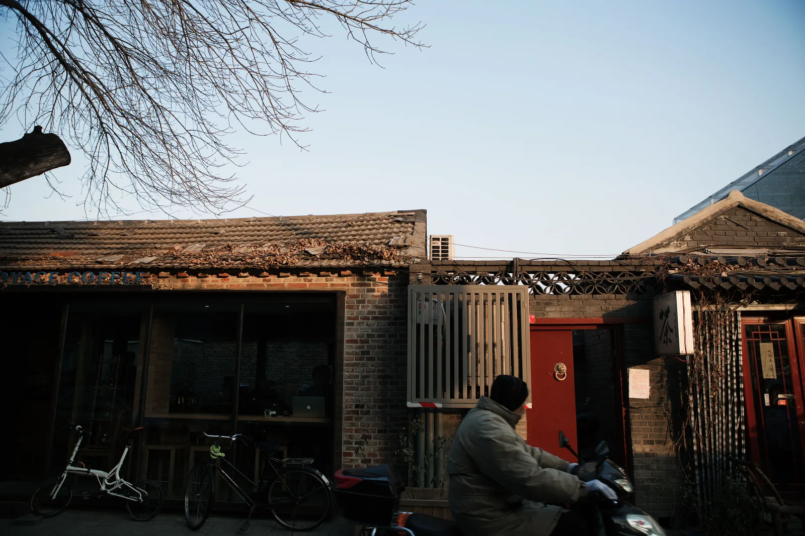 A resident riding through a lived-in Beijing hutong where old courtyard buildings meet everyday city life