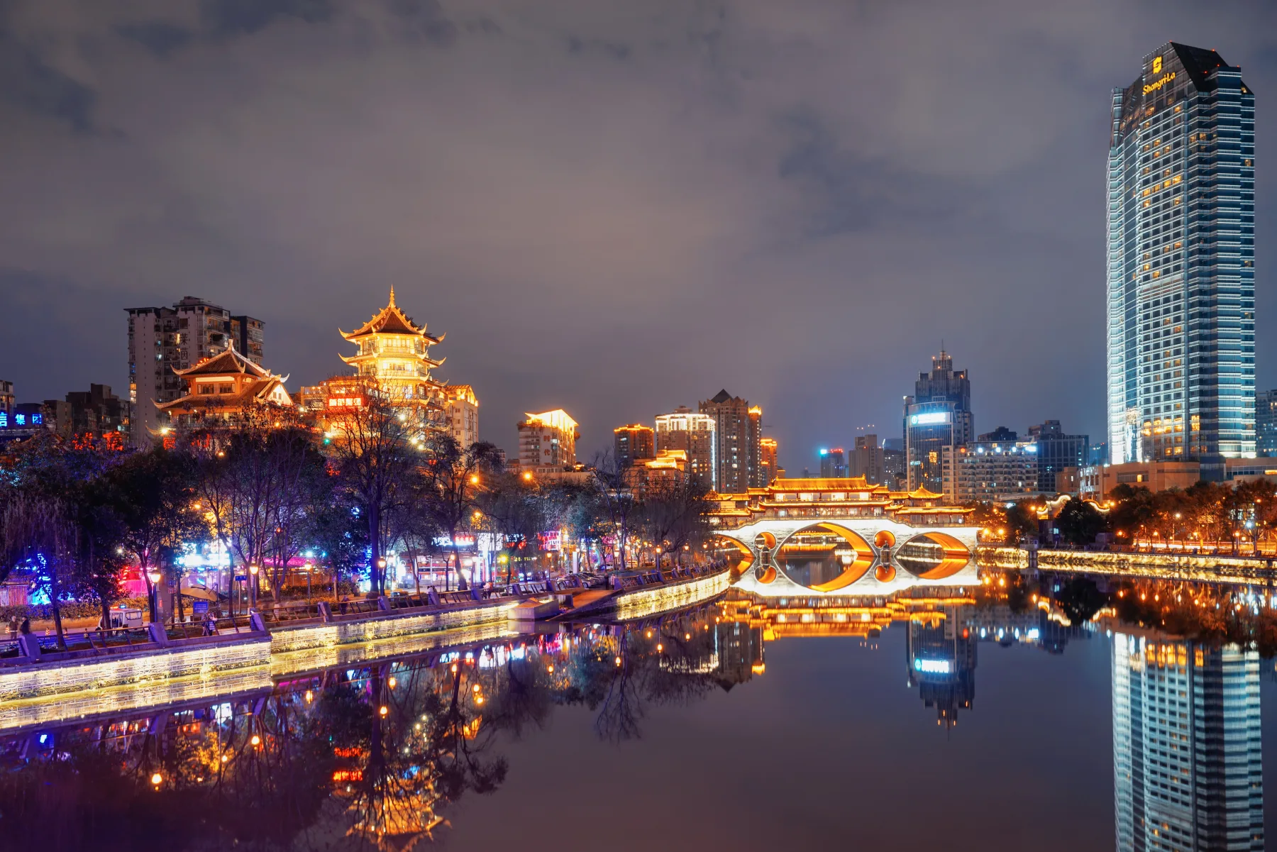 Illuminated Jiuyan Bridge and riverside buildings reflected in the water at night