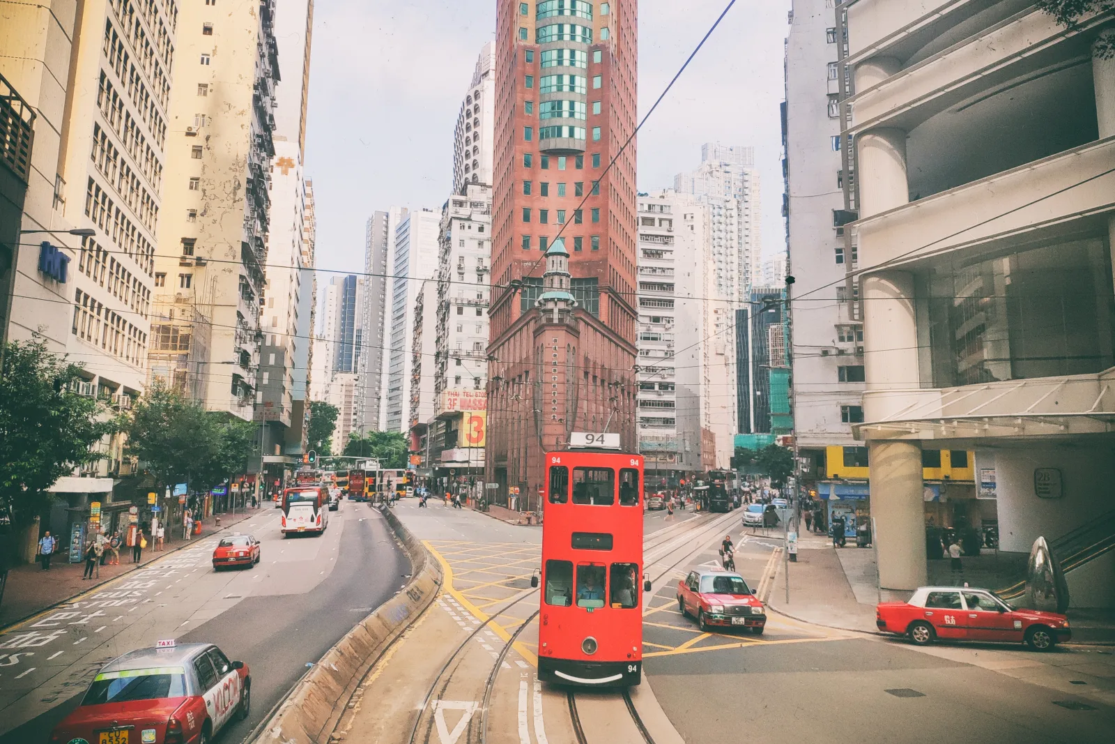 A red double-decker tram moving through an older Hong Kong Island streetscape
