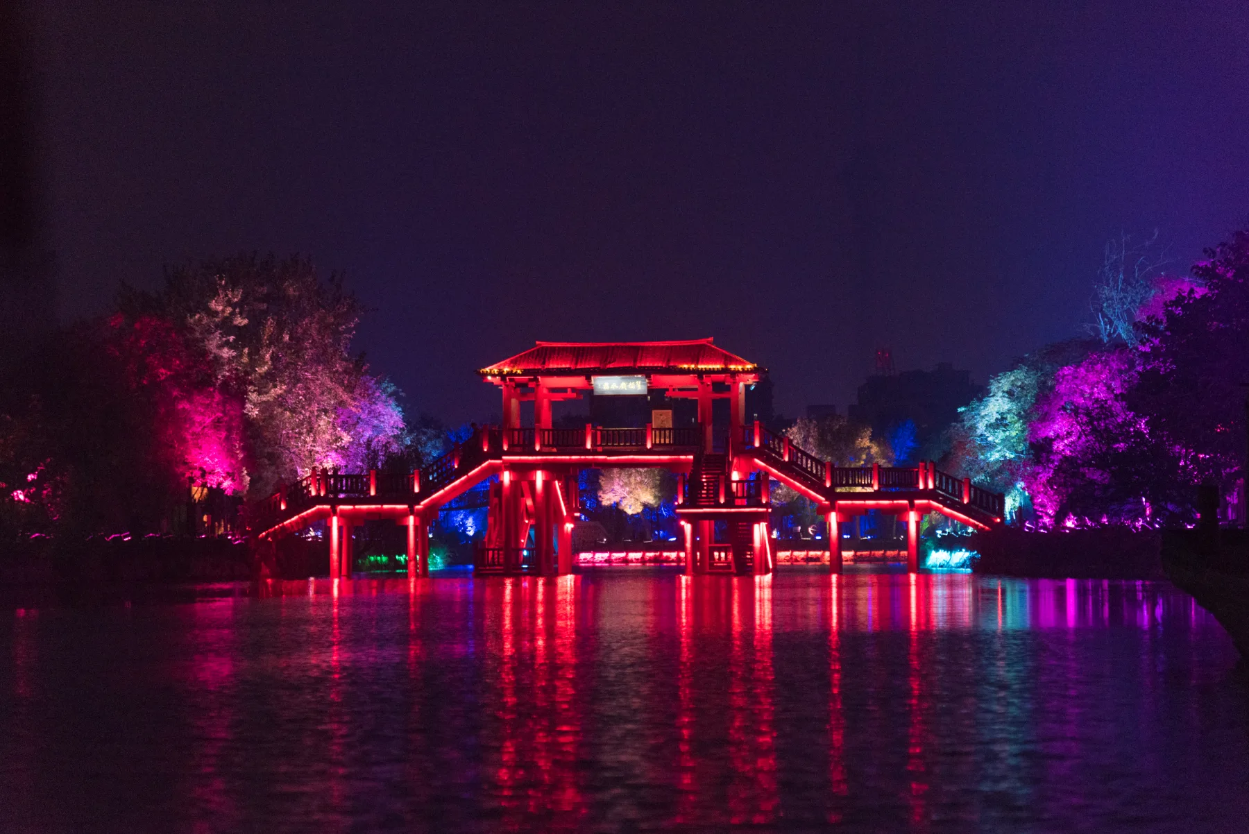 Illuminated bridges and pavilions reflected in water at Qingming Riverside Garden