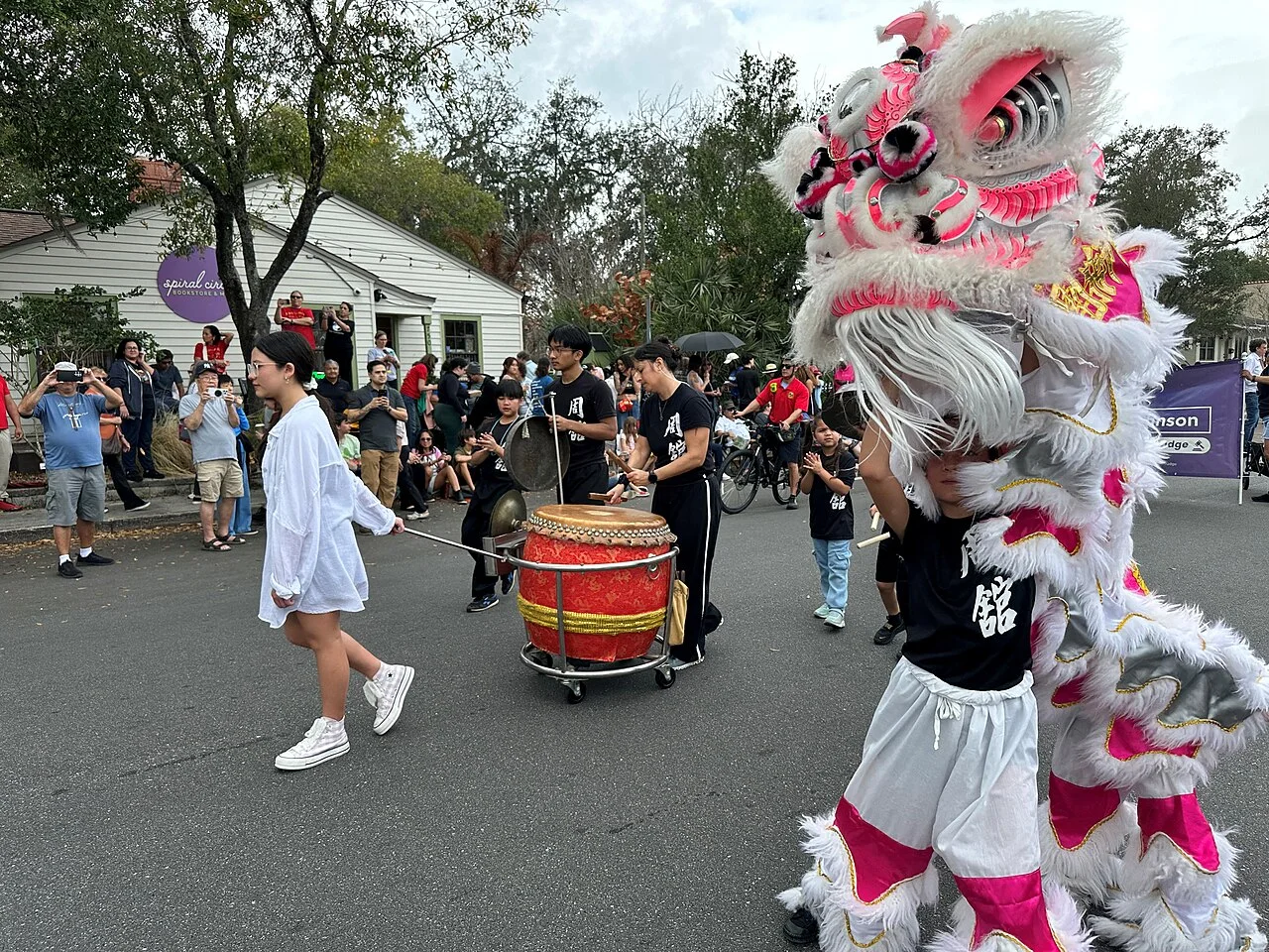 White lion dance performers moving beside a drummer and cymbal players