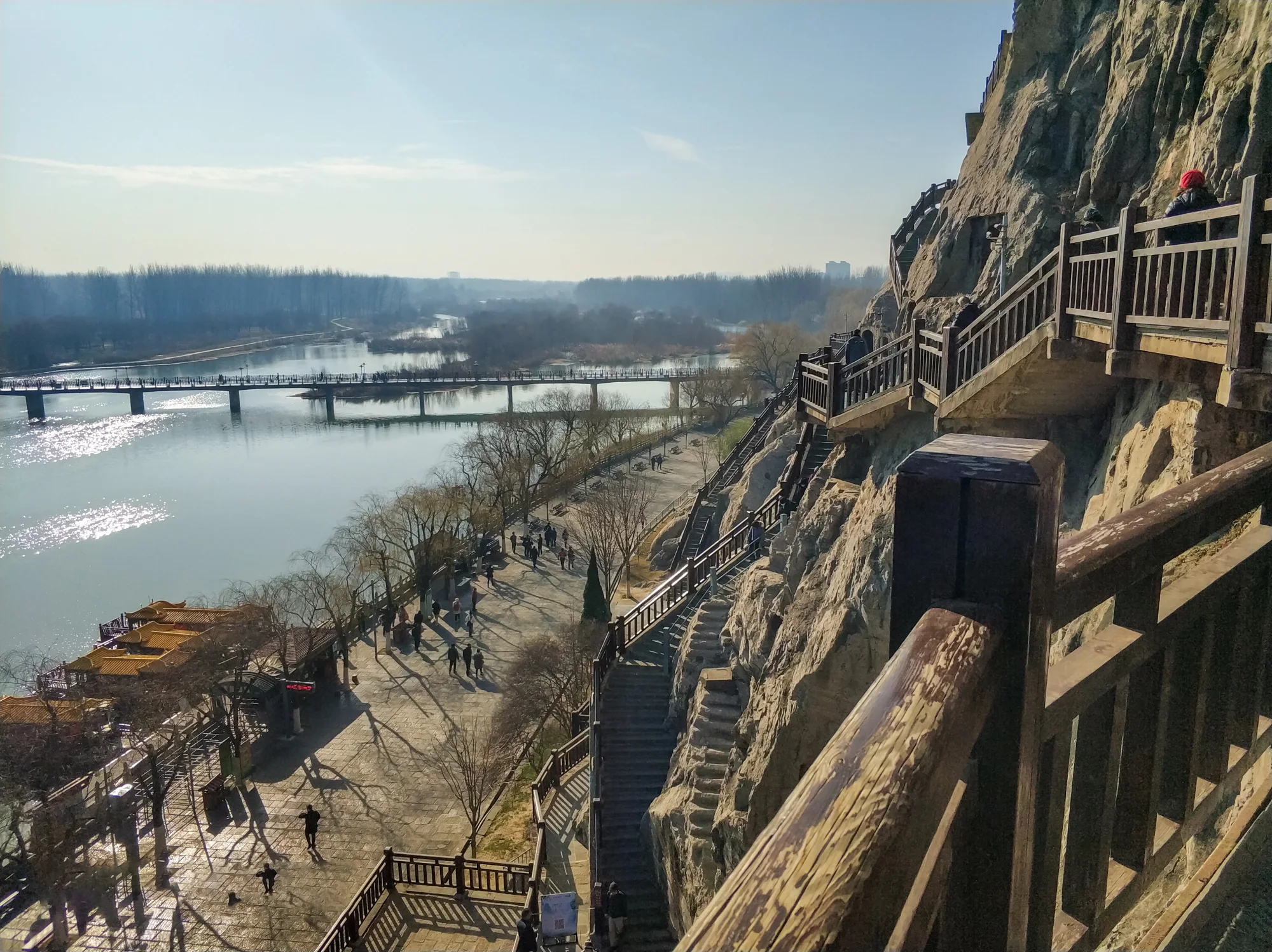 The Longmen cliff and riverside walkway showing the physical scale of a site visit