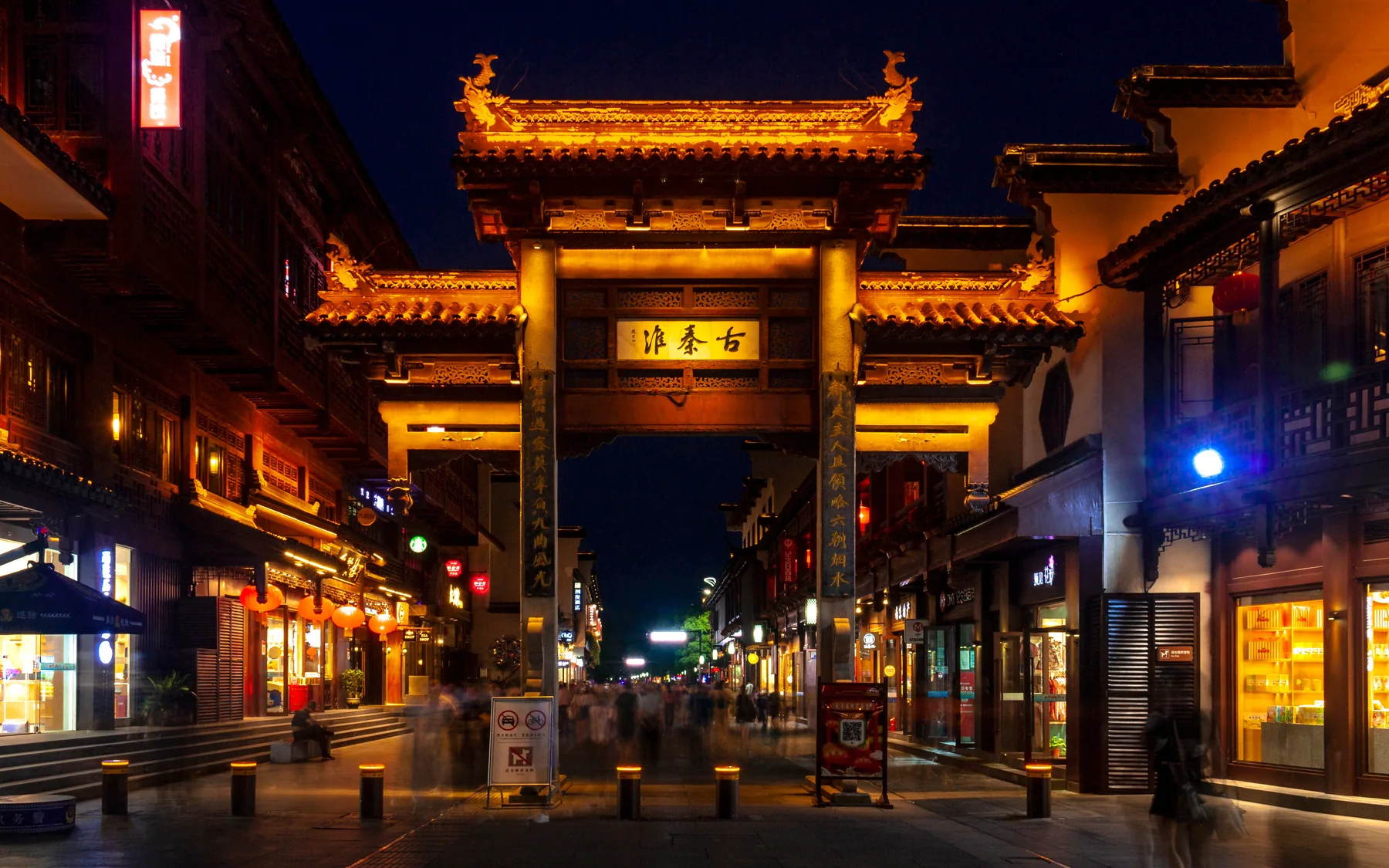 A brightly lit commercial street arch in the Fuzimiao district, showing how ritual memory now shares space with contemporary night commerce