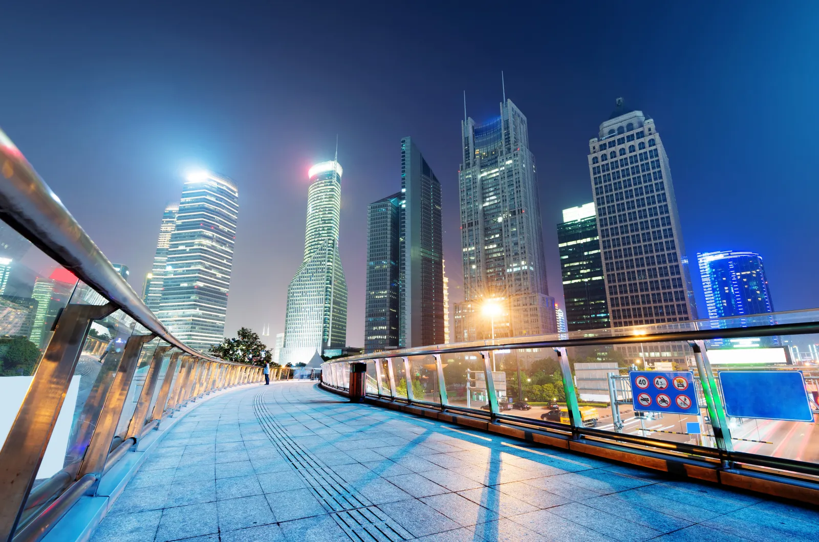 An illuminated pedestrian walkway passing between modern towers in central Shanghai