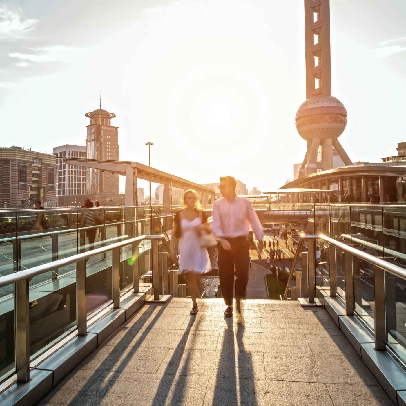Young adults walking through a sunlit public space in Pudong with the Oriental Pearl Tower behind them