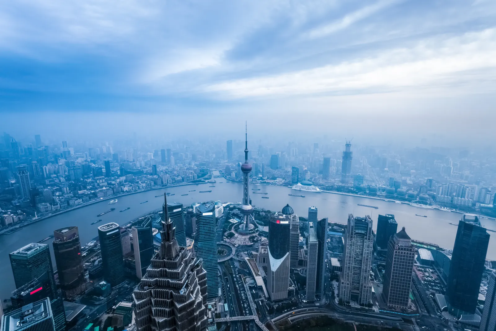 Shanghai seen from above with the Huangpu River, Pudong towers, dense neighborhoods and working boats visible together