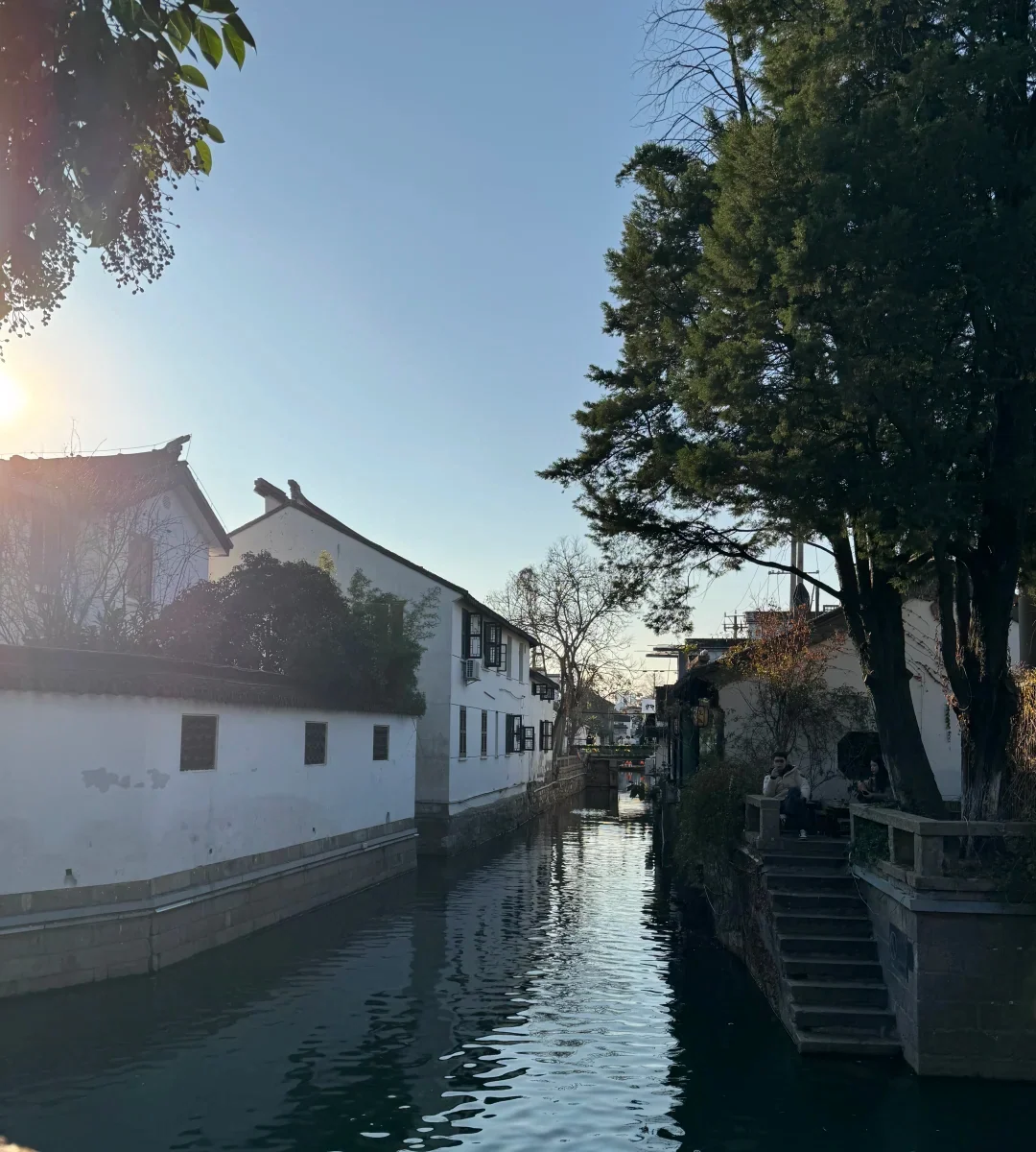 A quieter Suzhou canal lane showing residential frontage, trees and ordinary movement beyond the landmark streets