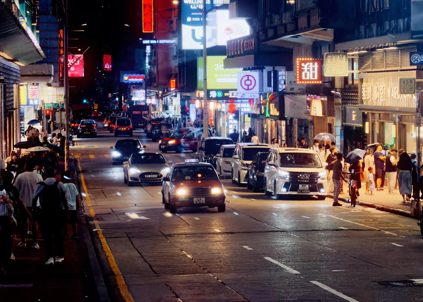 Traffic, pedestrians and stacked illuminated signs compressing a wet Mong Kok night street into several competing depths