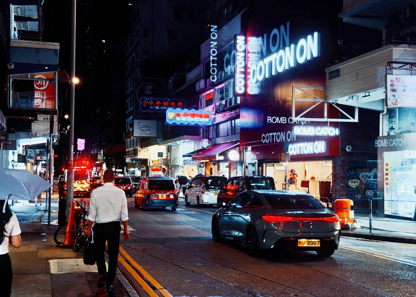A red Hong Kong taxi crossing a bright Mong Kok junction beneath stacked shopfronts and apartment facades