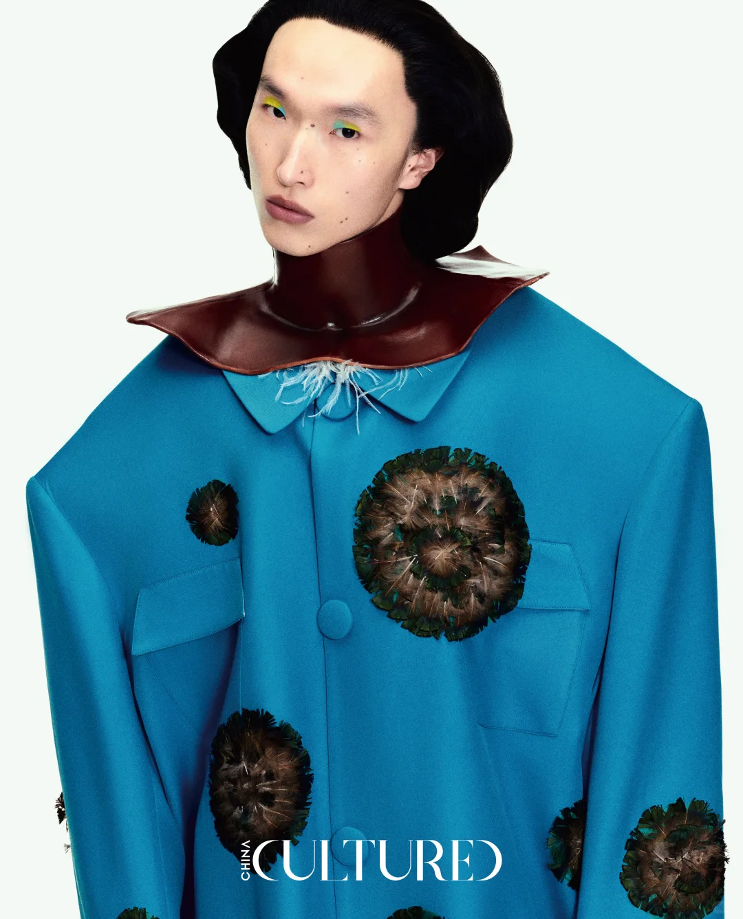 A model in sculptural blue outerwear with a rigid dark collar and dimensional circular surface details